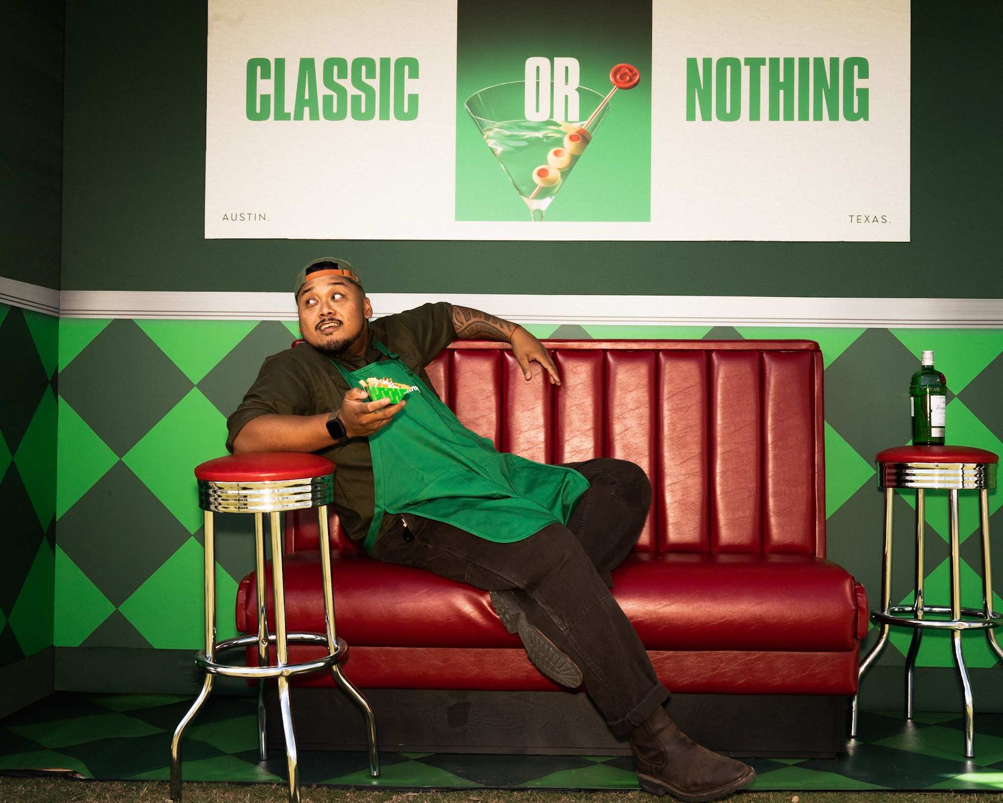 Portrait of a man in a green apron seated in a red diner booth